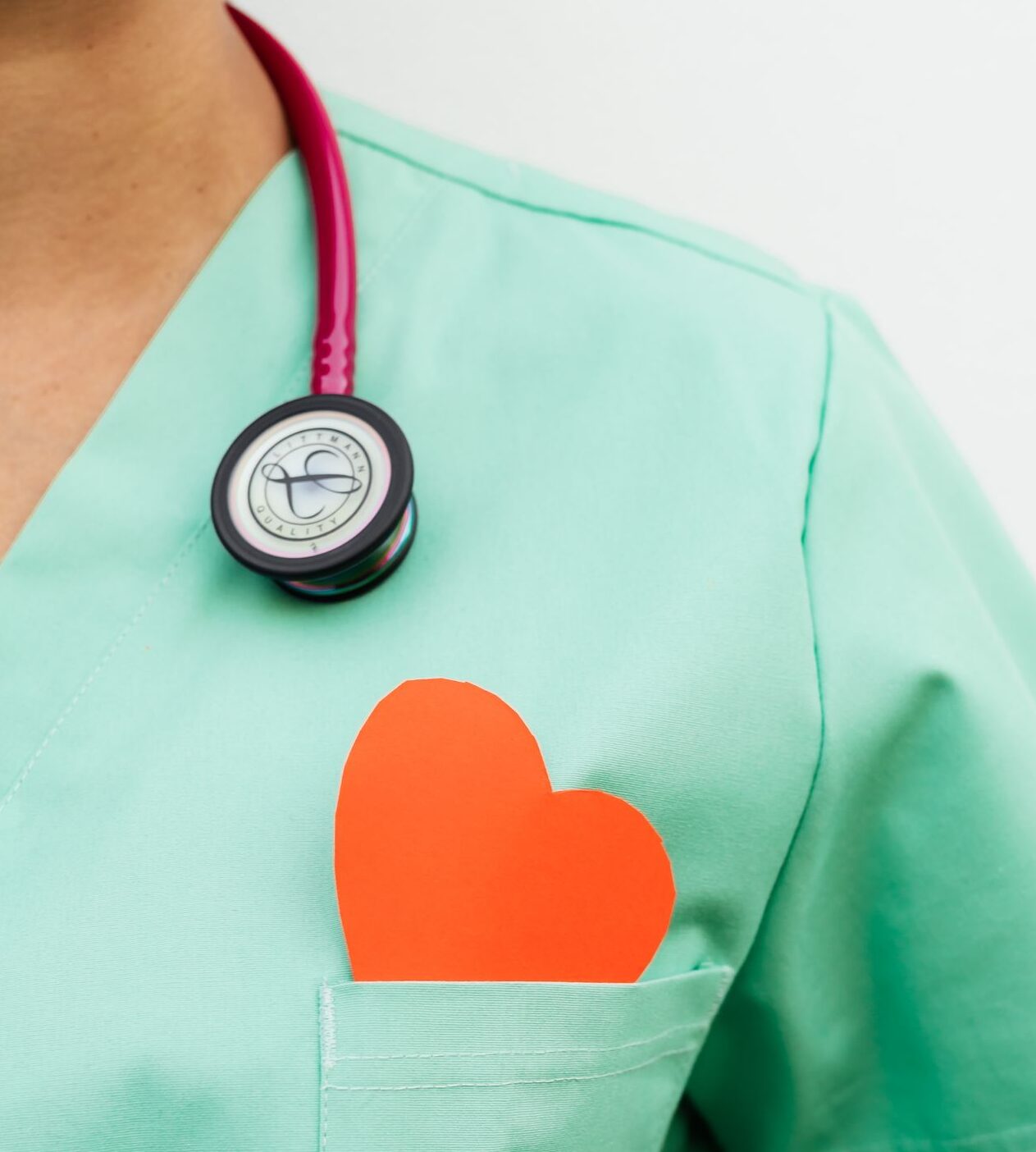 Nurse in pastel green scrubs with stethoscope and paper heart for heart health awareness.